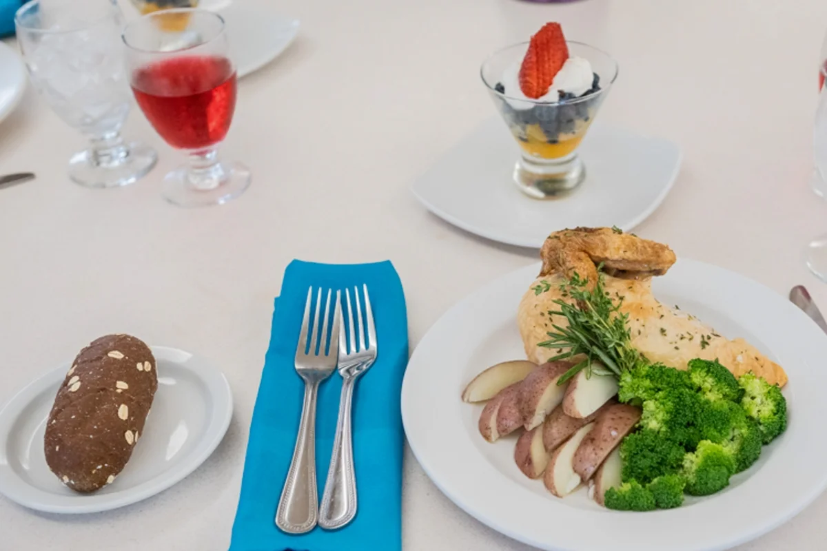 chicken dinner with bread, dessert cup, drink, and forks